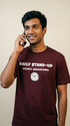 Man wearing a maroon t-shirt with text and a clock graphic, talking on a phone.