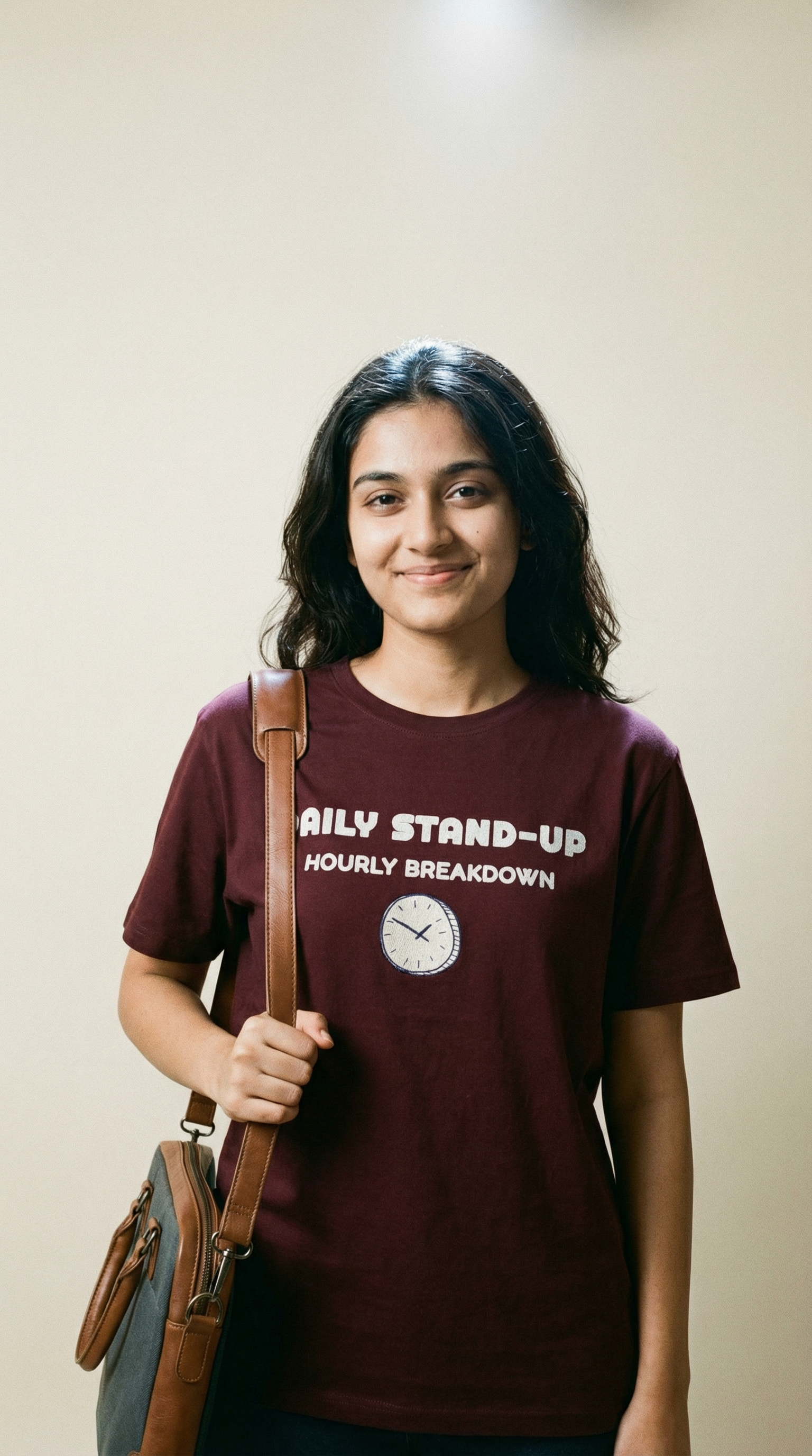 Person wearing a maroon t-shirt with text and a clock graphic, holding a bag against a plain background