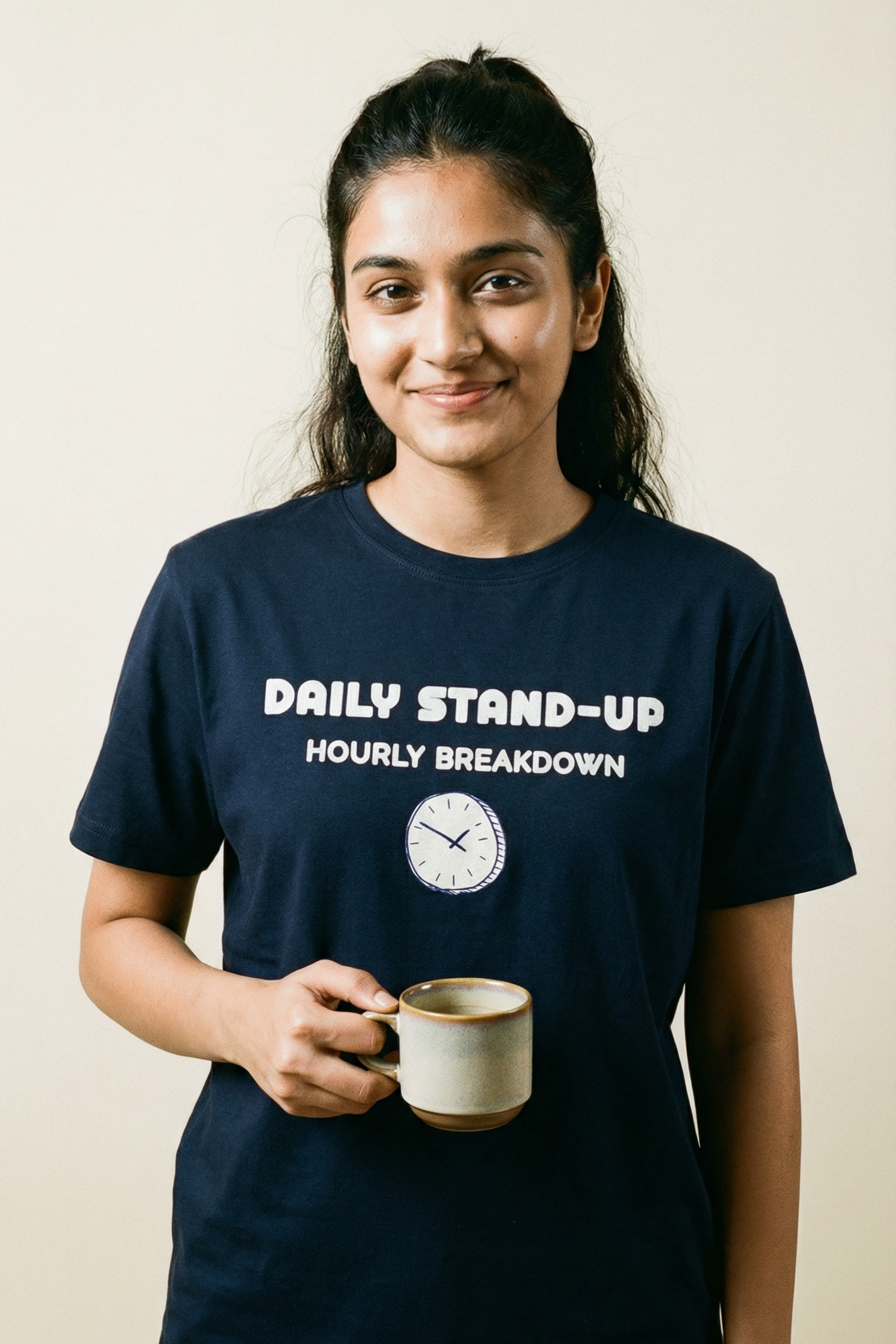 Person wearing a navy blue t-shirt with text and holding a mug against a plain background